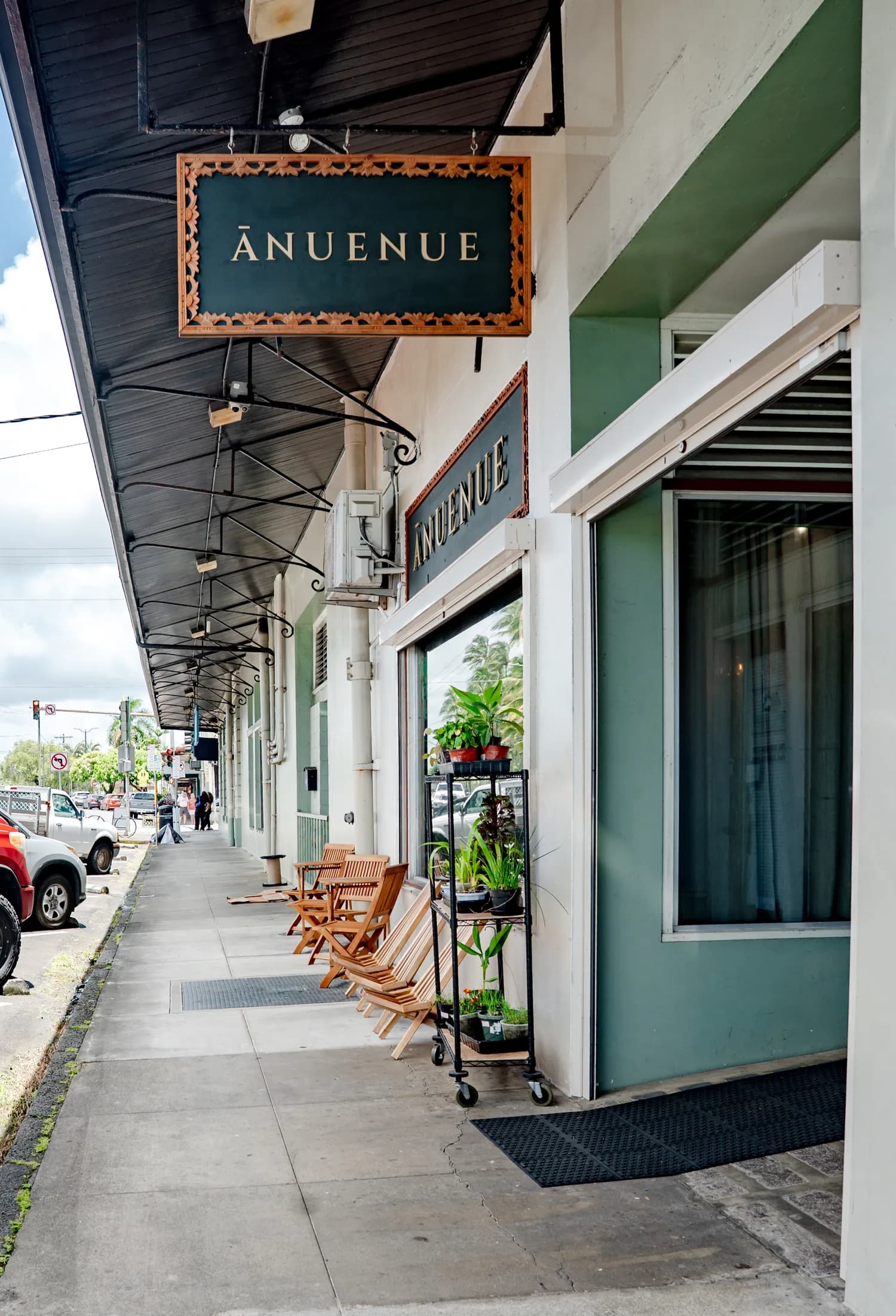 The green Ānuenue On The Bay storefront on Kamehameha Avenue, with the carved wooden Ānuenue sign hanging over the sidewalk